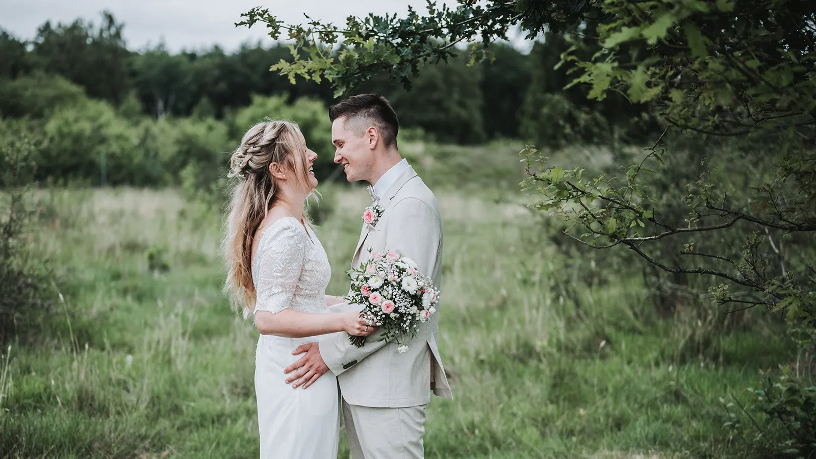 Lina und Johannes stehen Stirn an Stirn und lachen in einer Wiese am Waldrand bei Marne